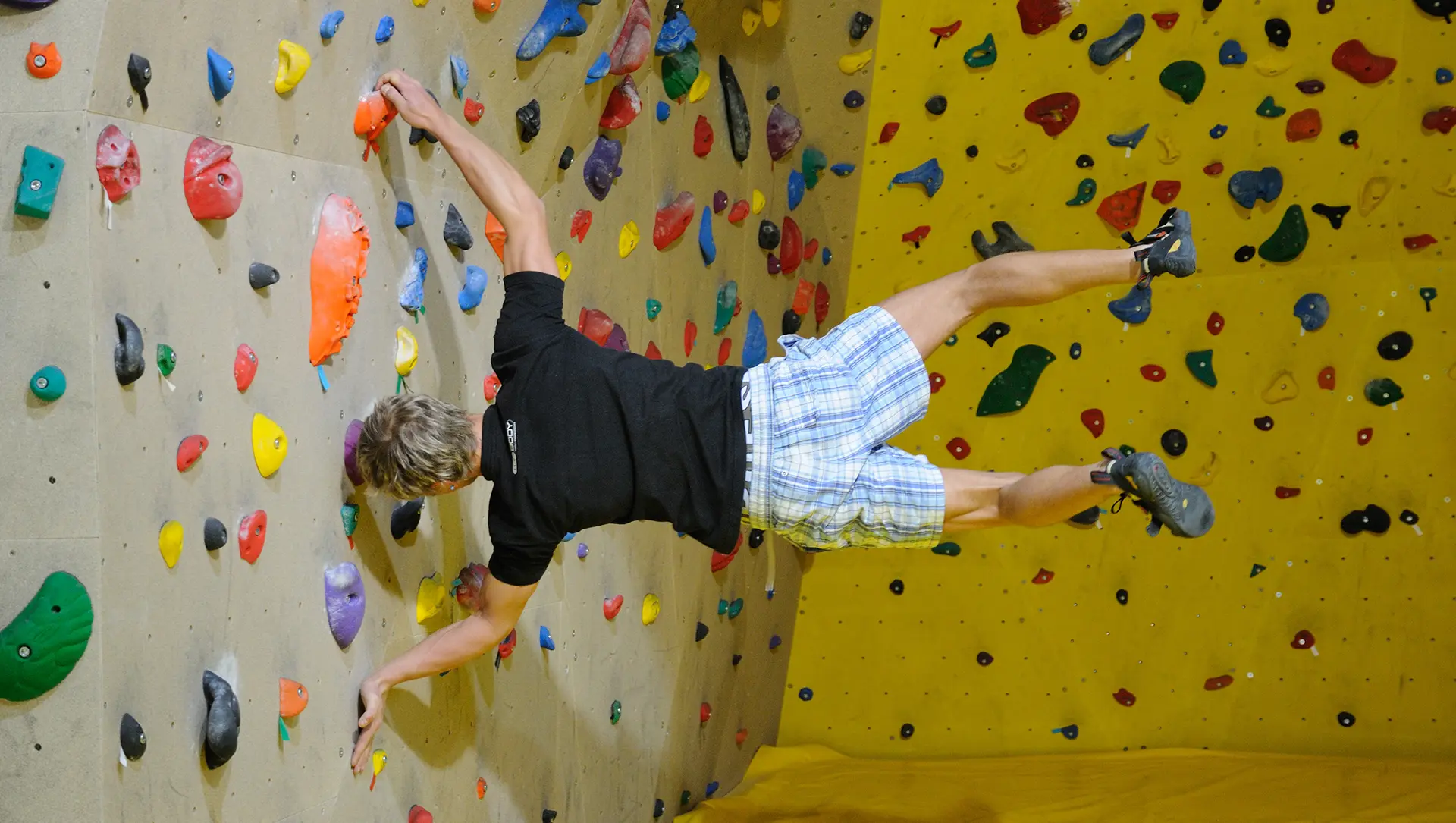 Hintergrundbild. Ein Mann hängt parallel zum Boden und hält sich an einem Vorsprung an der Wand