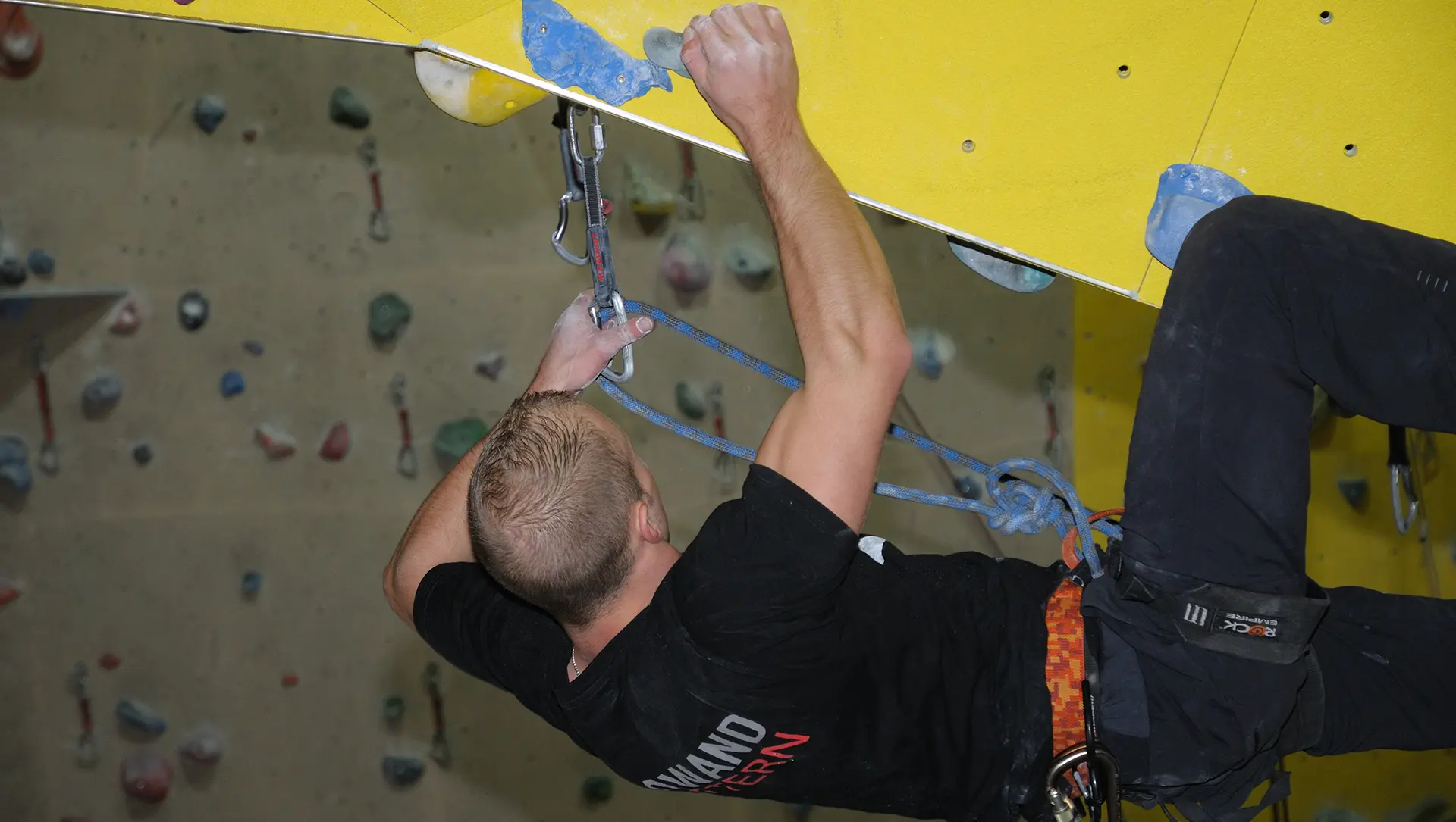 Hintergrundbild. Ein Mann klettert die Wand einer Kletterwand hinauf